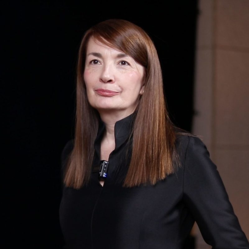 Dragana Ognjenović, poznata srpska modna dizajnerka, čeka početak snimanja intervjua na Zimskom Vivaldi Forumu. Ona je svedeno obučena u crno, uz blag osmeh, što je njen karakterističan modni izražaj. Pozadina slike je tamna, sofisticirana.